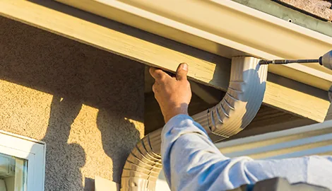 Hand fitting a white downspout elbow under a gutter outlet on a stucco house