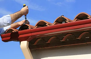 Installer fastening a hanger inside a red aluminum gutter along a roof edge