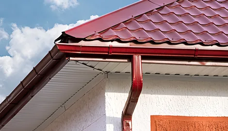 Red aluminum gutter and downspout installed along the eave of a house with a tiled roof